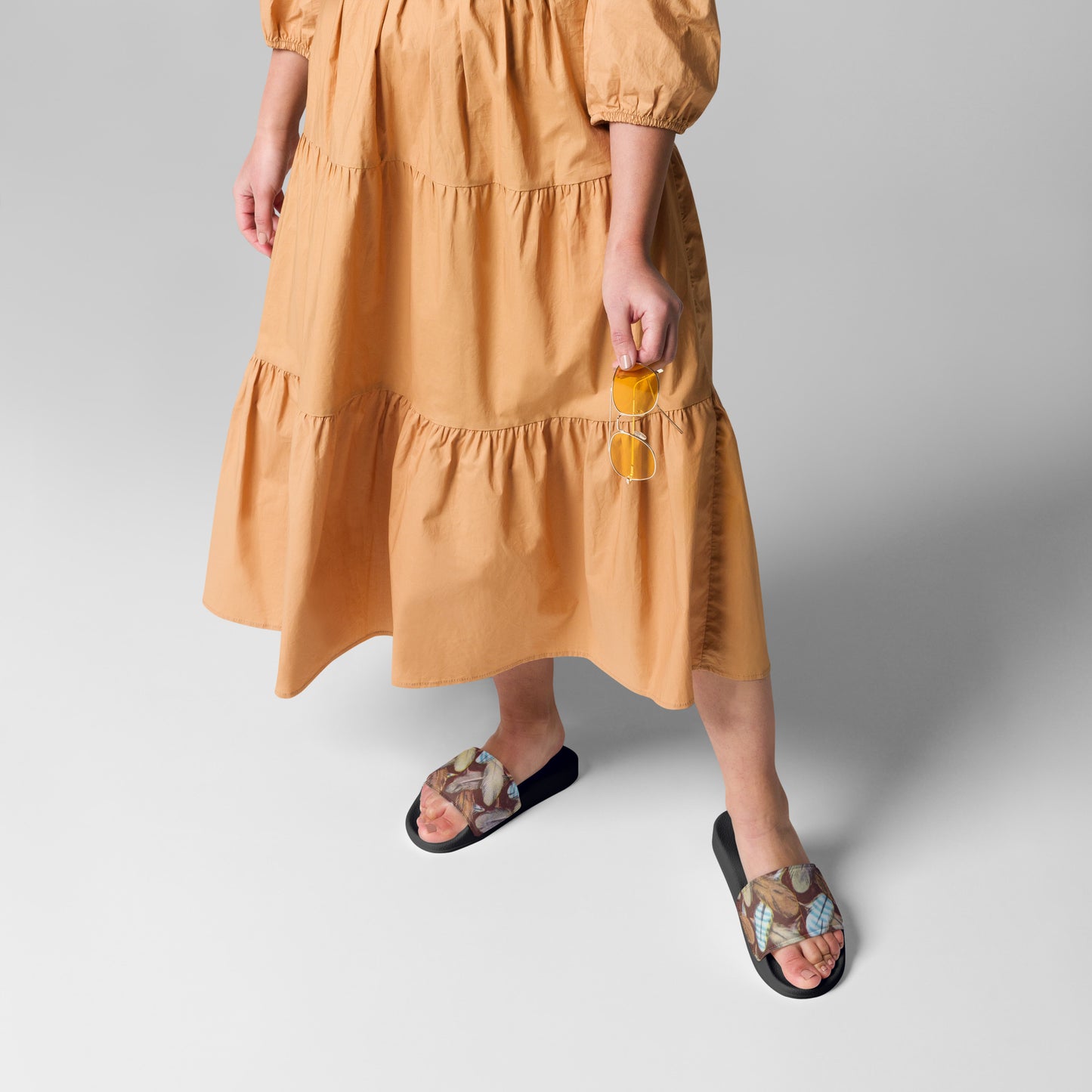 Person wearing a mustard yellow dress with feather pattern sandals on a light gray background
