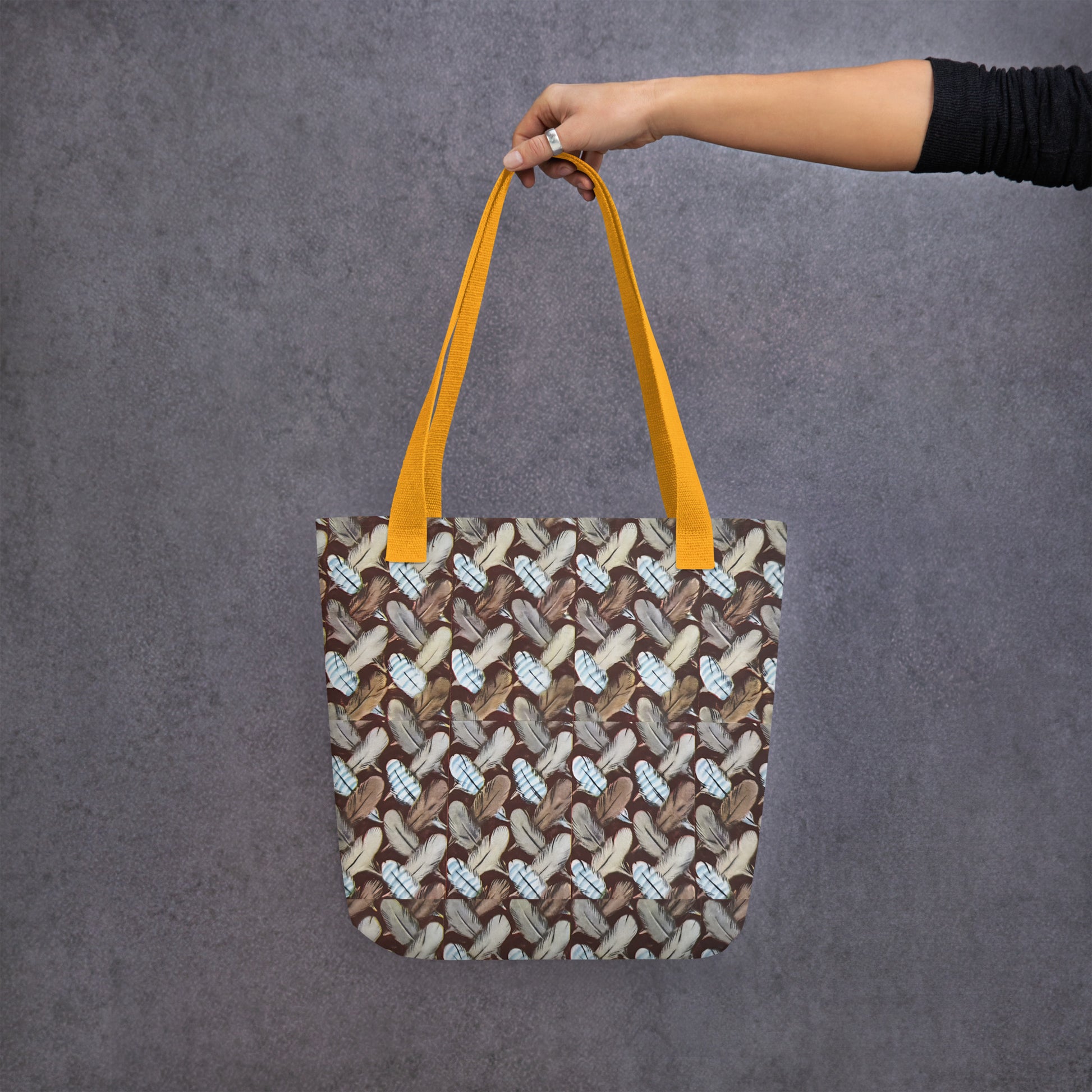 Tote bag with a feather pattern design held by a hand against a gray background