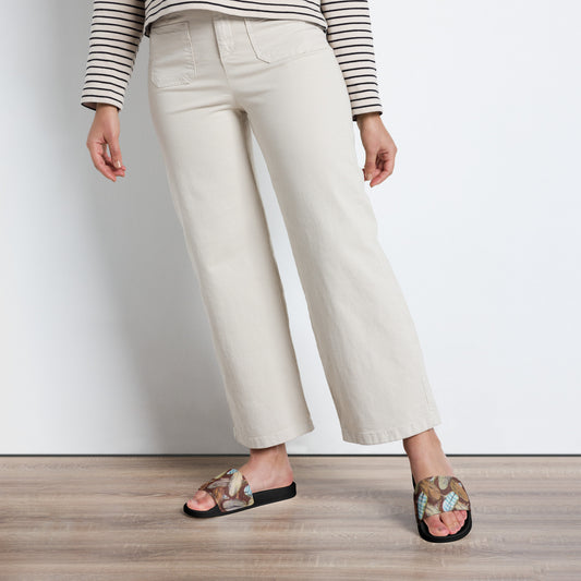 Person wearing white pants and feathermark feather pattern sandals on a plain background