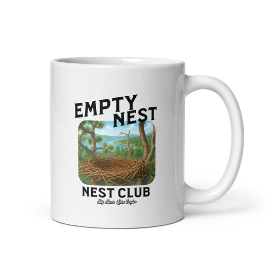 White ceramic mug with ‘Empty Nest Nest Club’ printed above an illustration of an empty bird’s nest perched high above a forest and lake. The design is playful and peaceful, evoking nature, quiet mornings, and birdwatching vibes.
