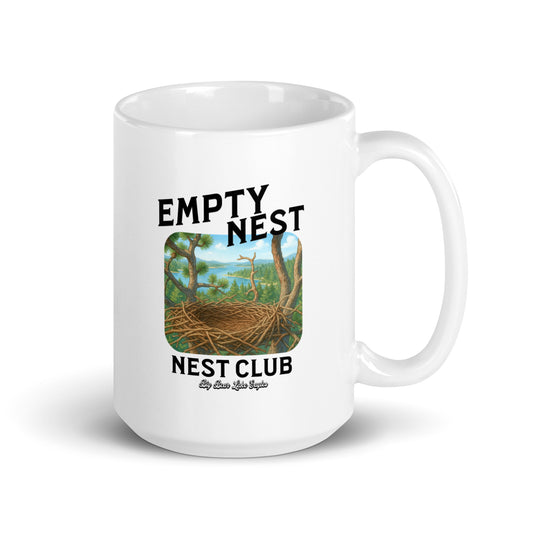 White ceramic mug with ‘Empty Nest Nest Club’ printed above an illustration of an empty bird’s nest perched high above a forest and lake. The design is playful and peaceful, evoking nature, quiet mornings, and birdwatching vibes.